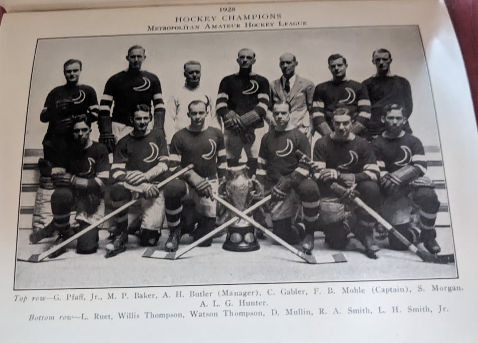 The Crescent club's ice hockey team, wearing dark sweaters with a crescent moon on the left breast, pose with their coaches in two rows (one kneeling, one standing) with their trophy front row center.
