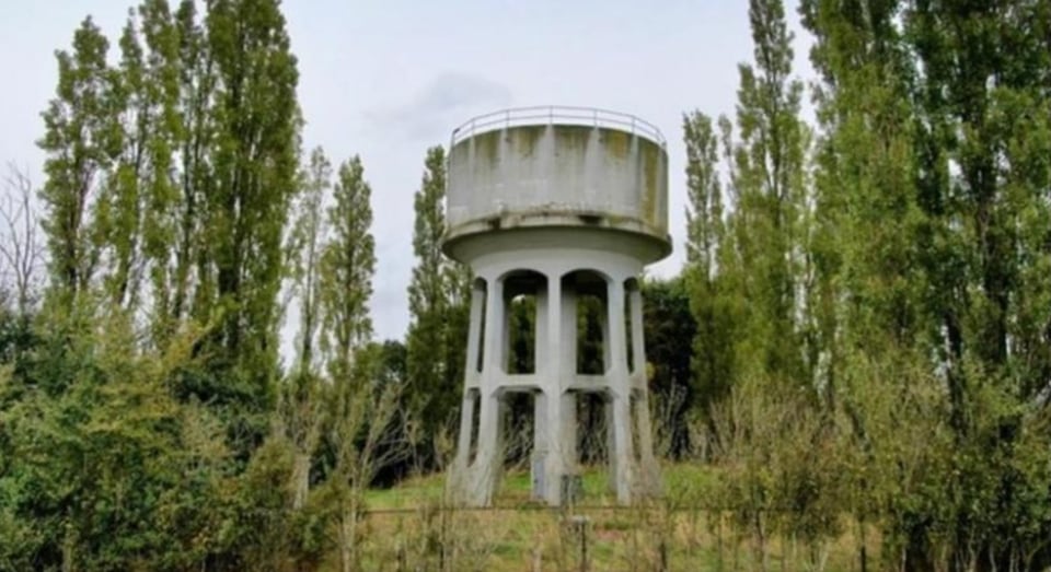 A slender concrete water tower surrounded by trees and overgrowth.