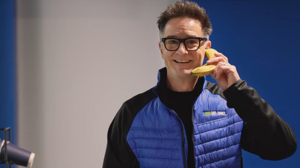 A dork in a tech-bro fleece vest holding a banana like it's a phone.
