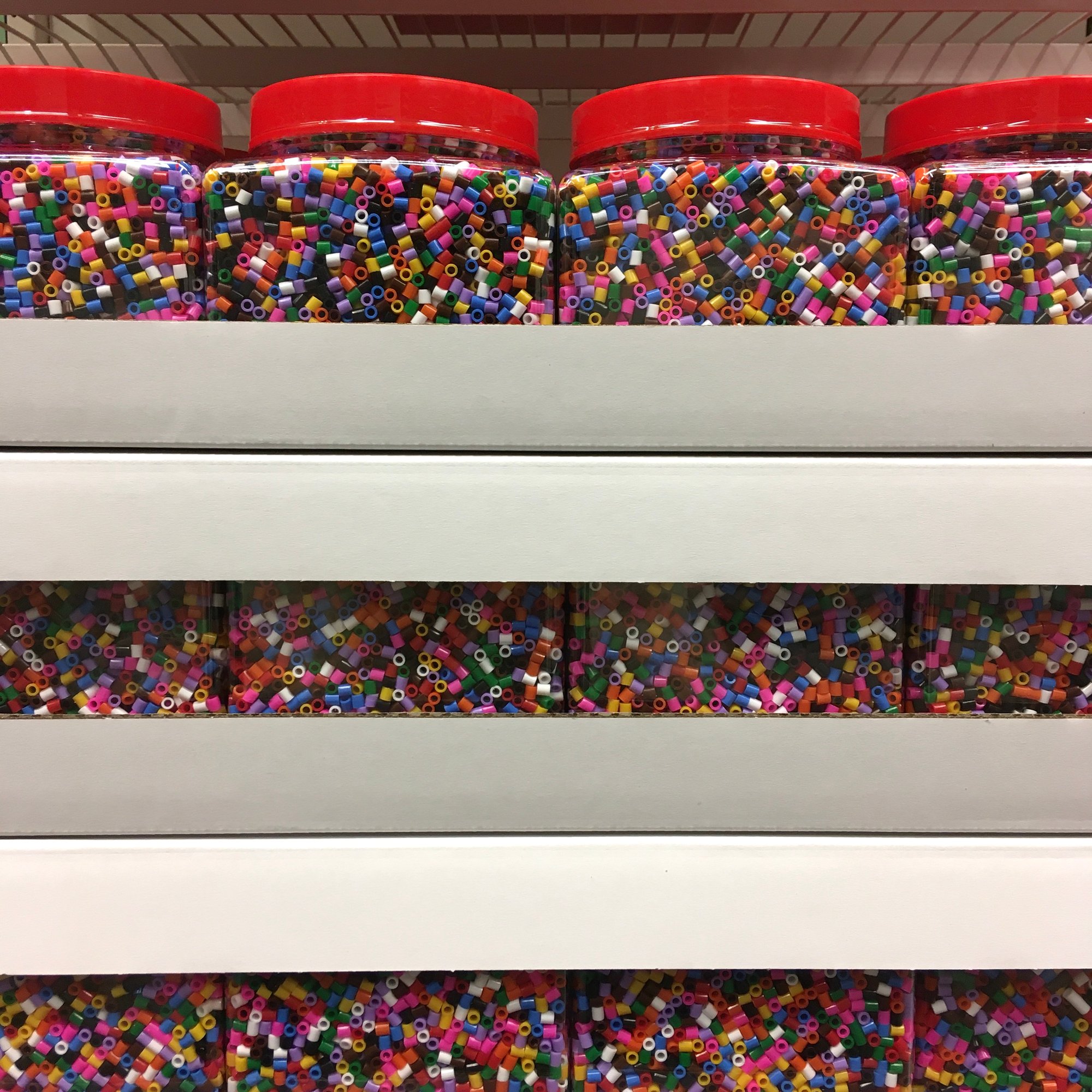 Photo depicts plastic jars of multicolored beads, stacked tightly on top of one another.