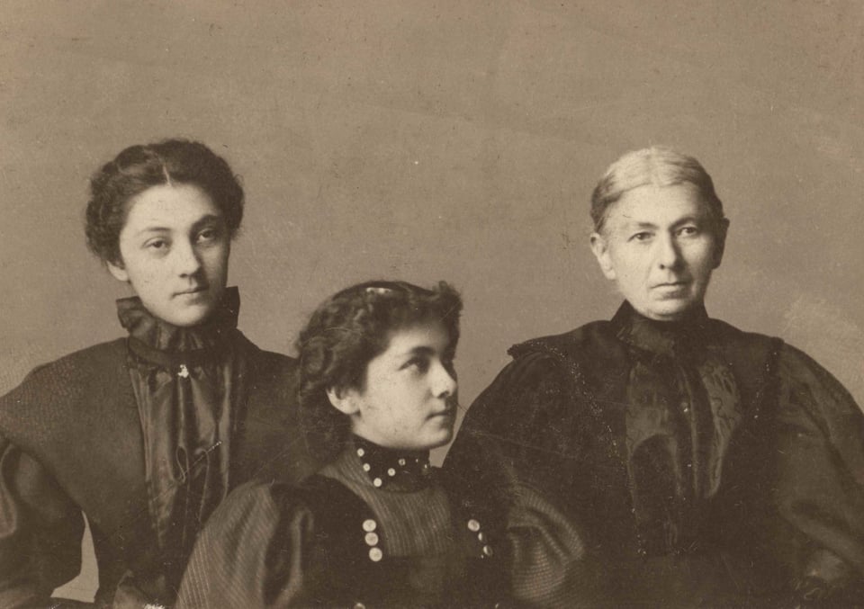 A black and white portrait photo of three women in dark dresses with puffy sleeves, taken around 1895.