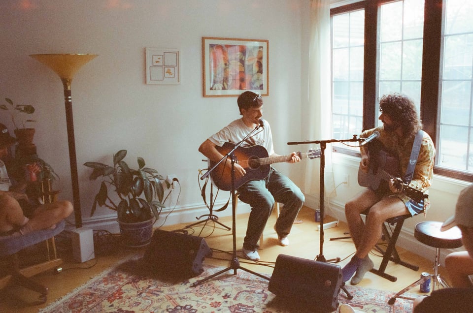 Jordan and Leche are both playing guitar, looking at each bantering in between songs