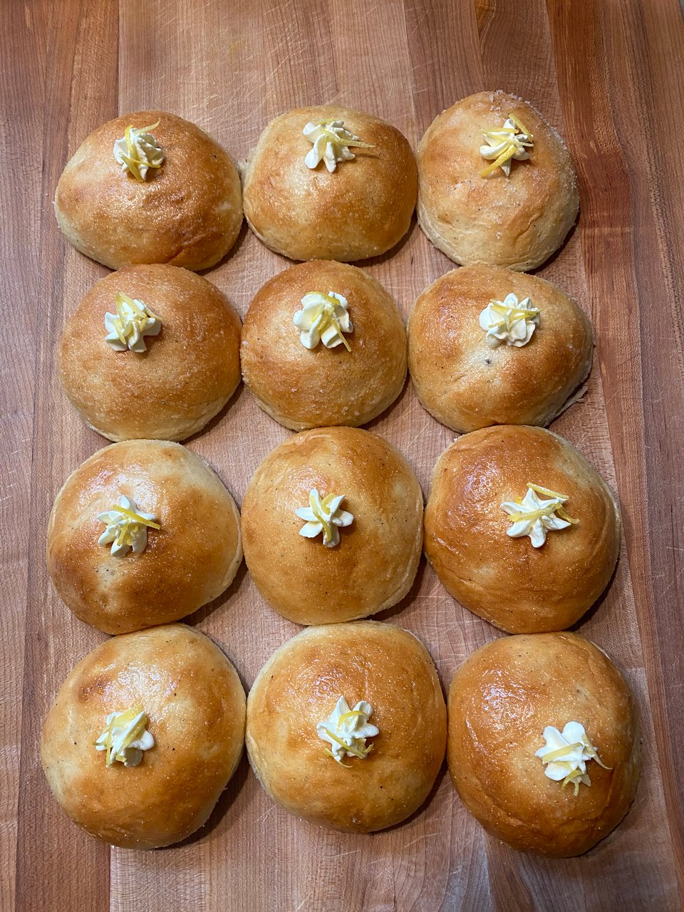 Twelve matching buns with a swirl of whipped lemon cream and lemon zest on top.