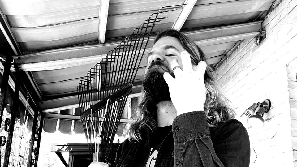 It's me, with long hair and beard, comically recreating the cover of Darkthrone's 'Pre-Historic Metal,' with a rake instead of a pitchfork.