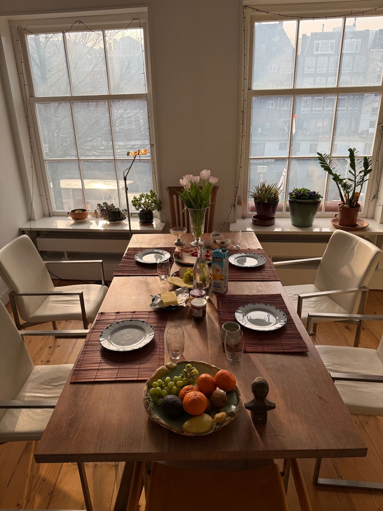 A table laid out with four place settings. There is a bowl of fruit and platters with meat and cheeses and bread and butter and jam.