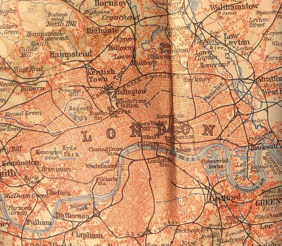 photo of a yellowed street map of London with the Thames winding through the middle, train lines marked, and buildings marked in red.