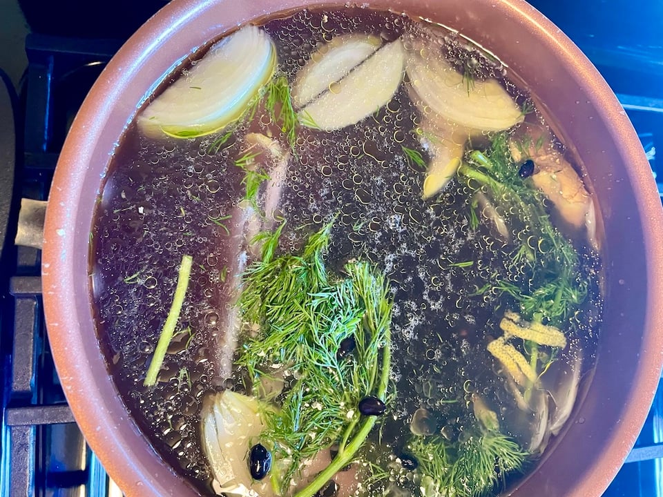 A pot with onions, dill and beans, with oil floating on top.