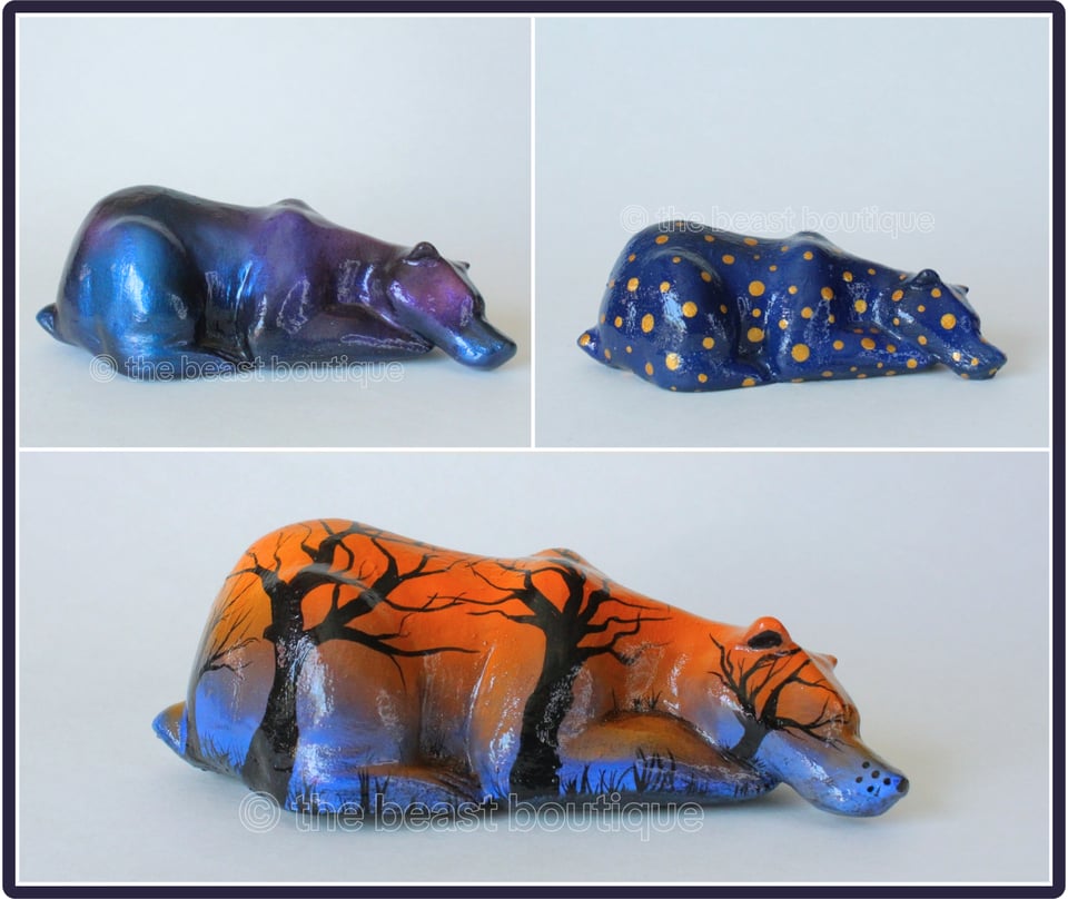 Three bear sculptures, laying down with gently sloped backs. Clockwise from top left: A Stardust Bear with glitterific metallic blue, purple and pink colors soflty blended for a skylike effect. Top Right is a Blue bear with gold dot pattern. Bottom most is an autumnal bear with a bright orange sky with the silhouette of leafless trees. Very October.

the shop name, the beast boutique, watermarks the image.