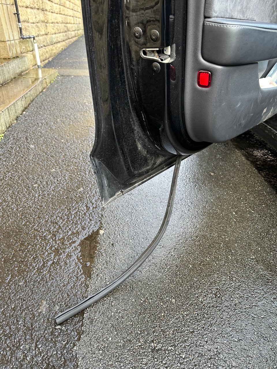 Image of an open door, with a rubber seal coming off the door, lying on the pavement.