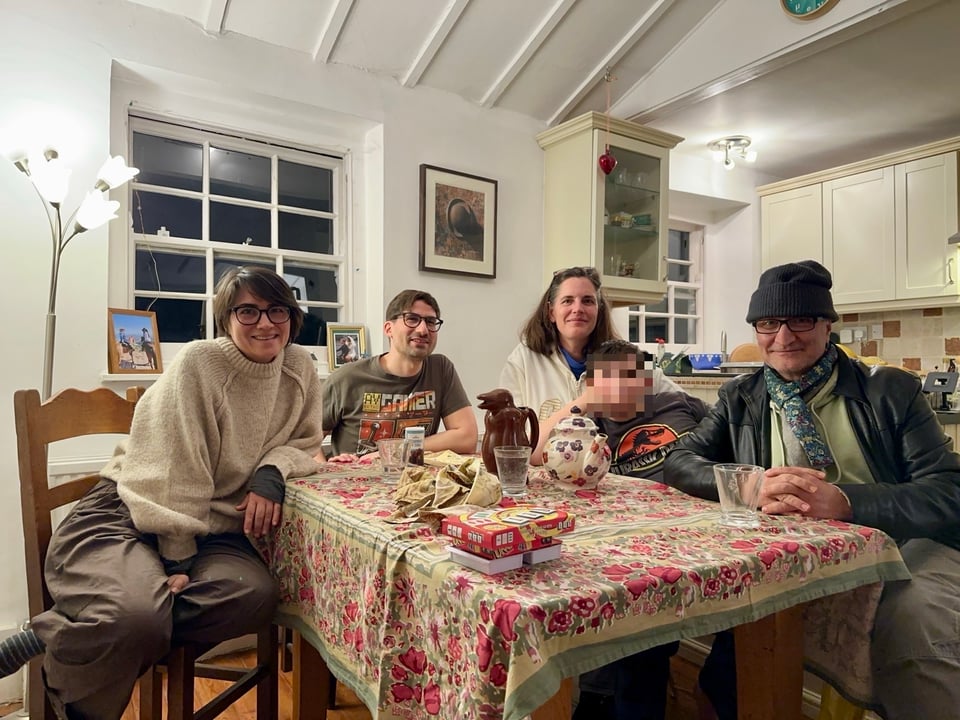 Five people sit around a dinner table. The child's face is blurred.