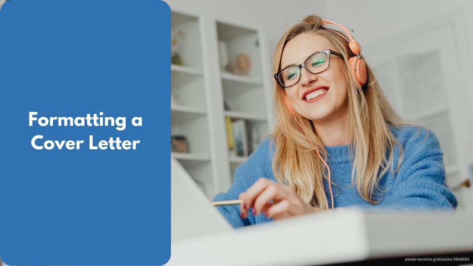 lady wearing blue sweater with earphones and using laptop on a white desk