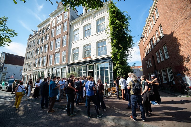 A crowd gathers in the street in front of a white canal house in Amsterdam.