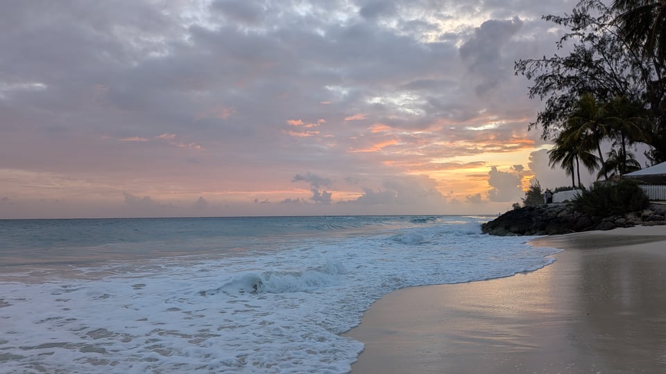 A beautiful grey-green sea under the apricot sunset and soft grey clouds. The light is reflecting off the wet sand.