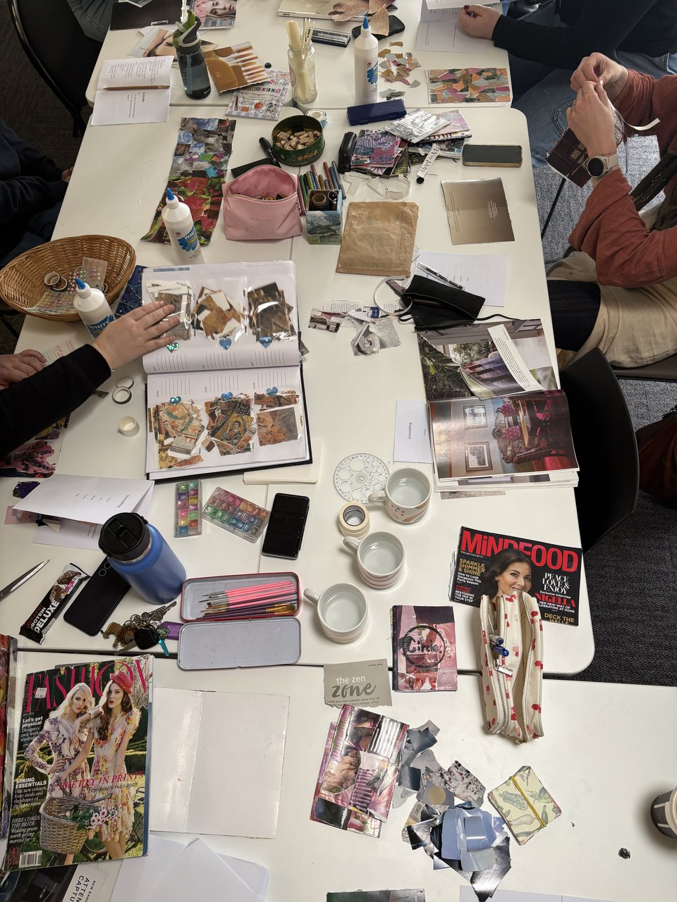 Bird's eye shot of a table of craft - anonymous participant arms and hands working on zines visible.