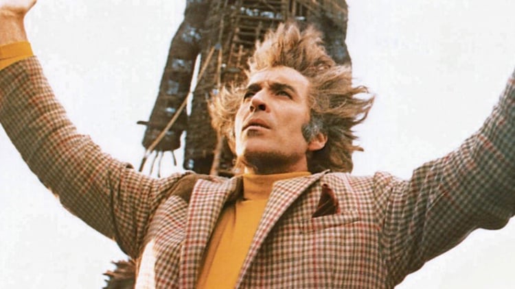 Christopher Lee has his arms raised in front of The Wicker Man.