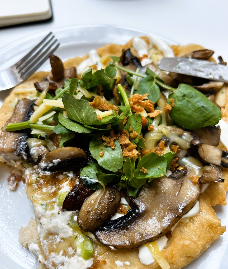 A flatbread loaded with mushrooms, cheese, yoghurt, salad and something crunchy.