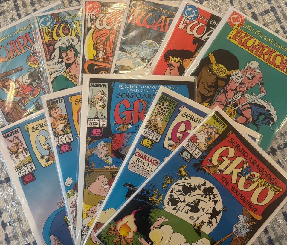 a handful of Warlord and Groo comic book back issues spread out on a table