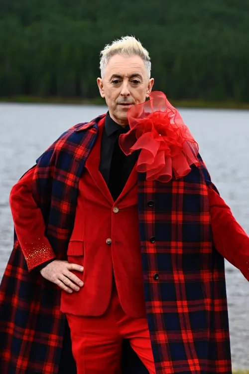 Alan Cumming in a red suit and red tartan coat