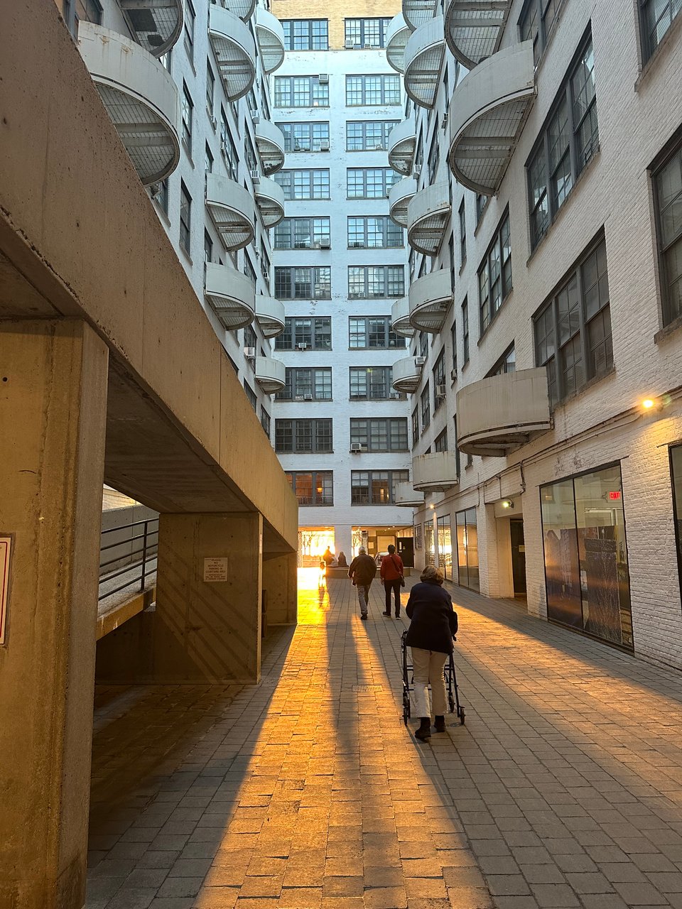 Photo of courtyard of Westbeth Artists Housing, with golden sunlight streaming through a low entryway, and long shadows of people