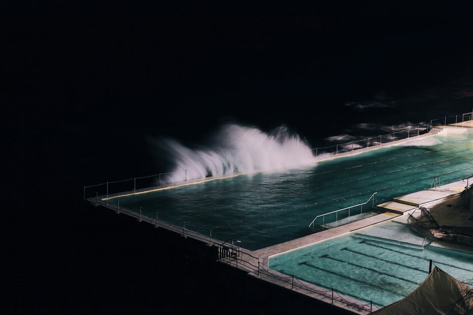 At night, a stormy sea wave splashes into a lap pool