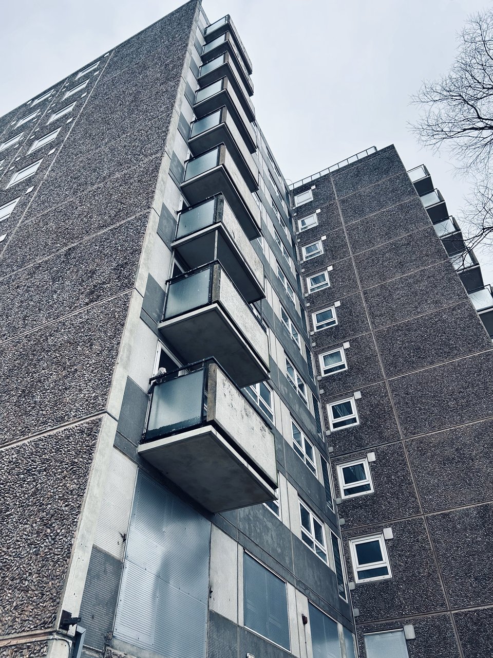 Looking up at the suspended balconies from below. The panel construction can be clearly seen, with end walls made of rough concrete and side walls tiled. The balconies show signs of moss or mould.