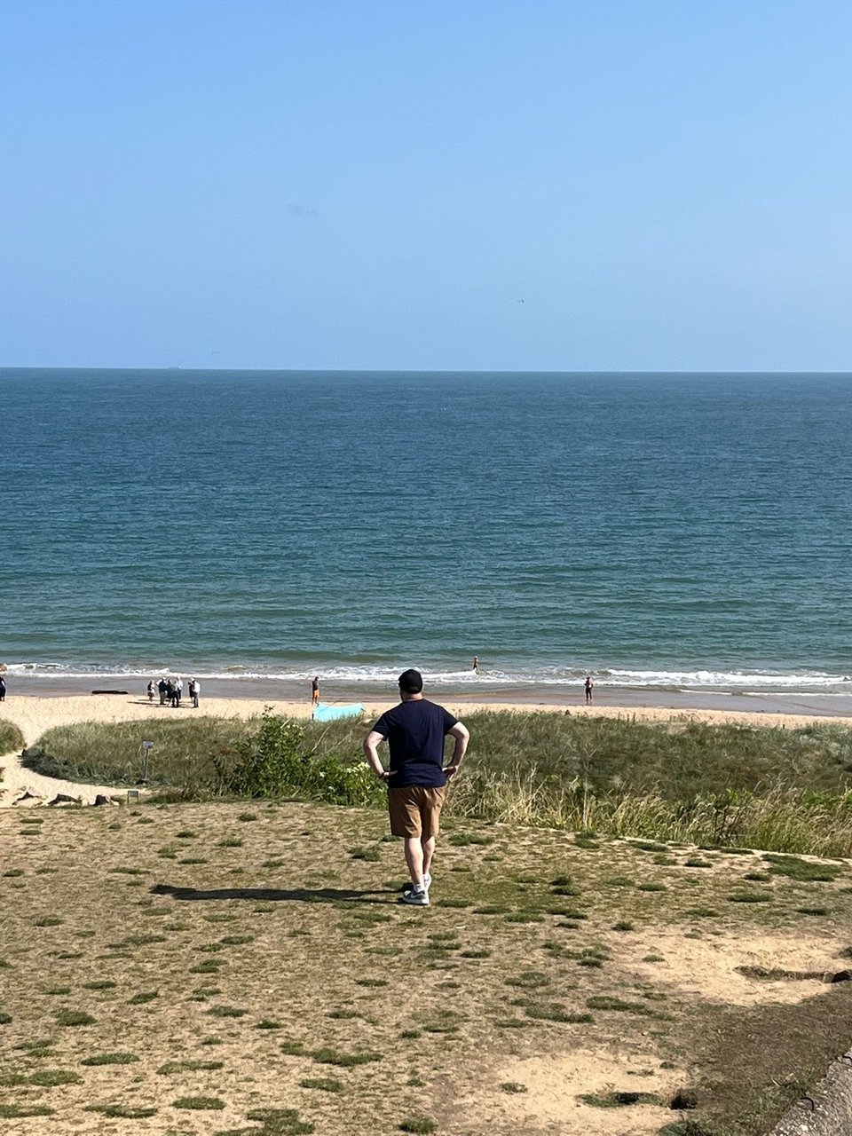 Neil standing with hands on hips atop a gun bunker, looking out on Omaha Beach