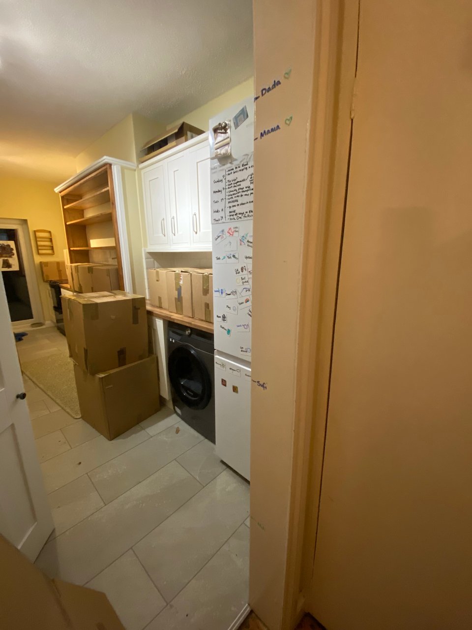 view of a galley kitchen with all stuff packed into boxes. On the door frame there are different heights marked with names Dada, Mama, Sufi and Meli