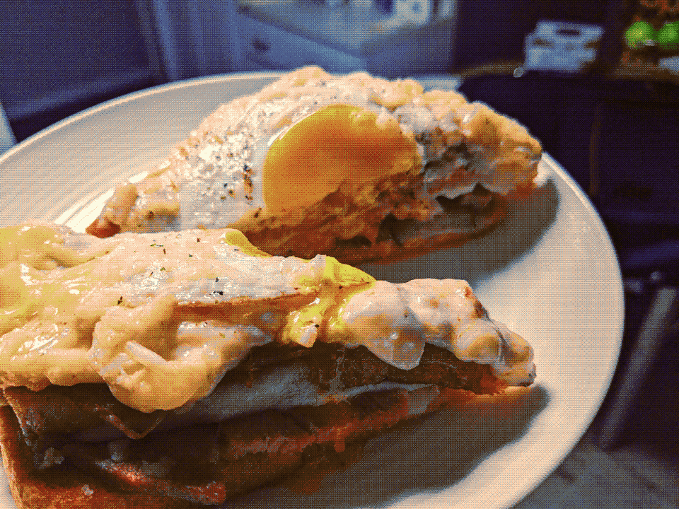 A ham-based sandwich on a plate, sliced in two and slathered with bechamel and topped with egg.