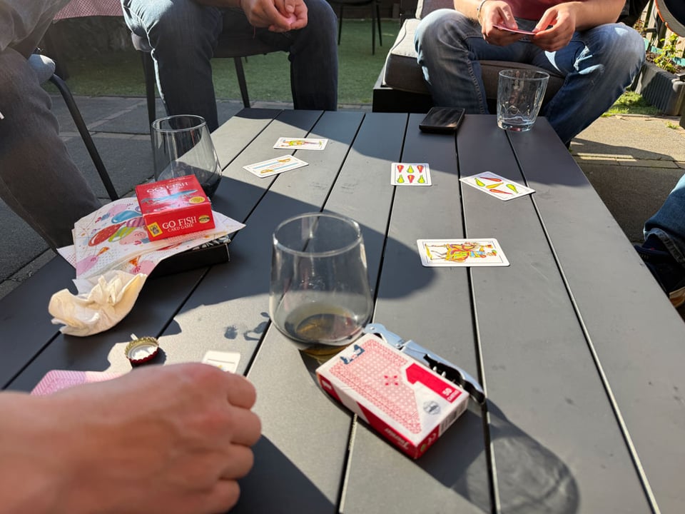 Close up of people playing truco at a table with empty glasses of drinks in the sunshine.
