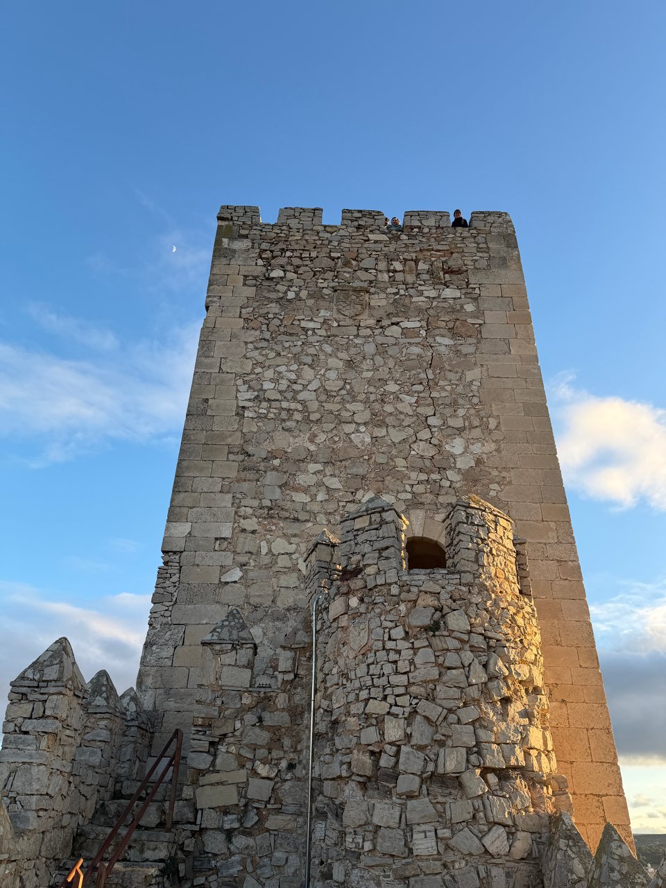 Two people look down from the top of a keep of a Spanish castle.