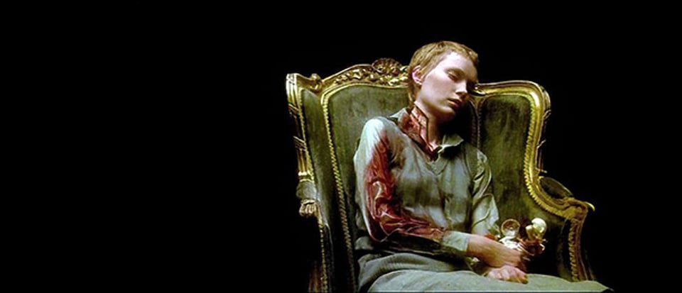Mia Farrow sits in a darkened room in an elaborate gold-and-green antique chair, right arm and neck bloodied from an injury.