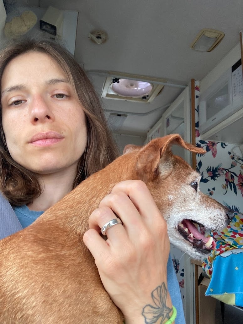 Meredith in 2023 holds Heidi in her lap, scratching her neck. We both look a bit greyer.