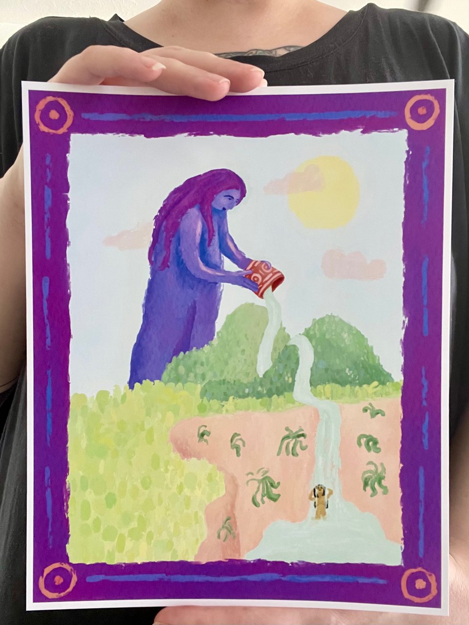 Photo of Destiny holding an illustrated print of an ancestor spirit pouring water, creating a waterfall that a human is bathing in.