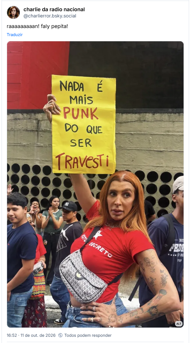 Post de charlie da radio nacional (@charlierror.bsky.social): raaaaaaaaan! faly pepita! (artista pepita nas manifestações pró-Lula na paulista com uma placa amarela escrito "nada é mais punk do que ser travesti" com destaque para as palavras "punk" e "travesti". ela tá usando uma camiseta vermelha e tem uma bolsa transversal pendurada)