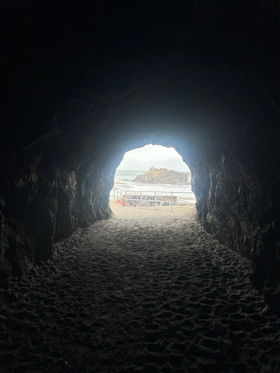 View from inside a dark cave opening, framing a sandy beach and ocean beyond.