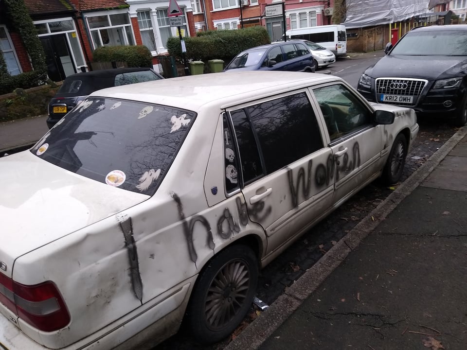 A white, quite battered car, with "I hate women" written on it in black spray paint