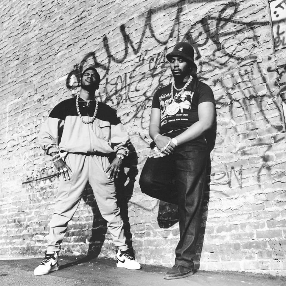 Eric B and Rakim stand against a graffiti-tagged wall