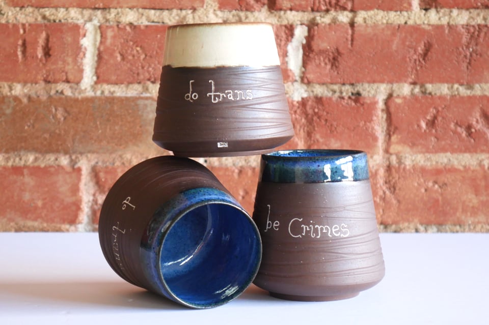 A stack of dark-brown clay tumblers with blue or white glazed rims, inward-sloping textured walls, and a rounded base with a foot ring
