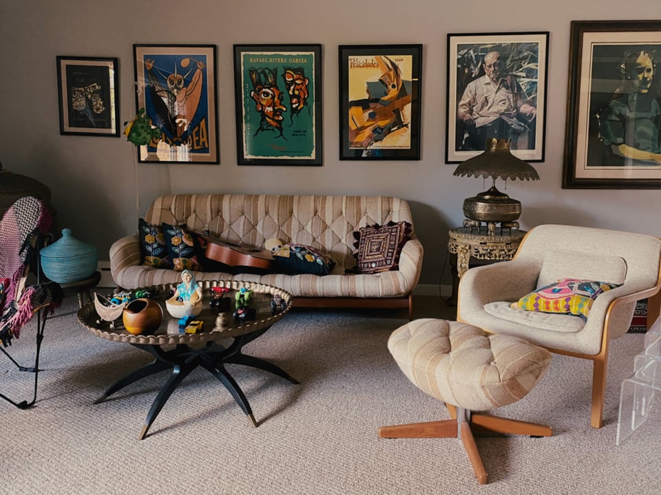Cozy vintage living room with a tufted sofa, patterned pillows, guitar, and eclectic art. An upholstered chair and unique round table enhance the warm, artistic vibe.