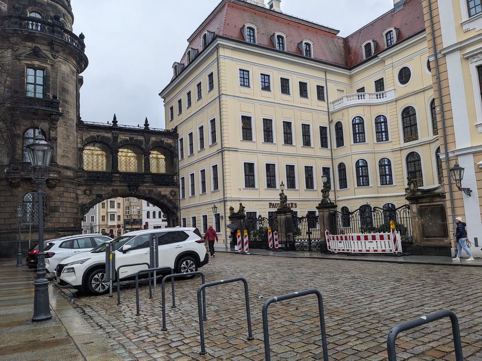 On the left is the former Royal Residence, a blackened sandstone structure (turret-like) with a similarly blackened sandstone bridge connecting it to the Taschenberg Palace on the right. On the right is a very clean, recently renovated structure with fresh yellow (plaster?) walls. The much older sky bridge attaches directly to the new building.