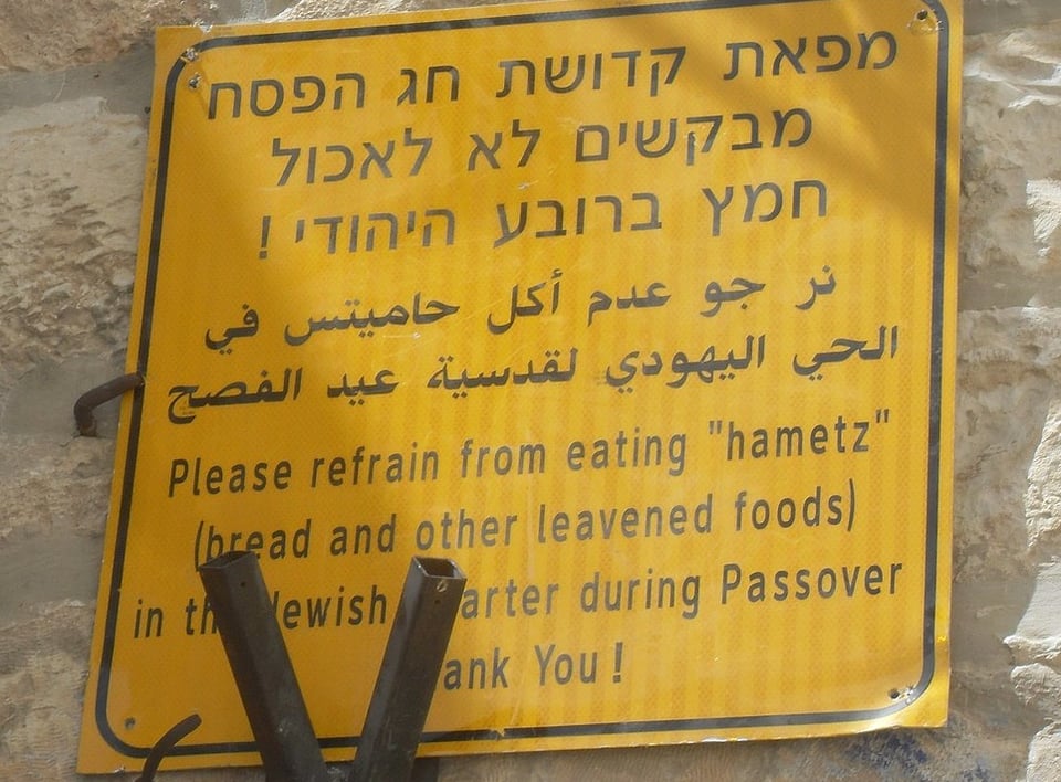 A sign in Jerusalem in Hebrew, Arabic and English. The English text reads: Please refrain from eating “Chametz” (bread and other leavened foods) in the Jewish quarter during Passover. Thank you!