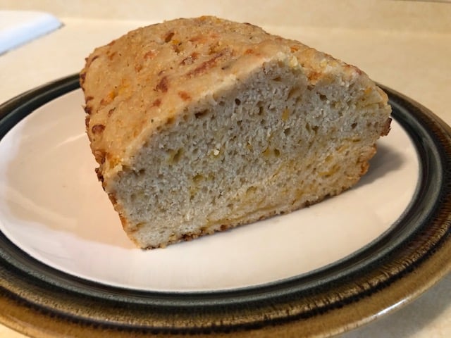 A loaf of cheddar garlic beer bread, sliced end facing the camera, on a plate