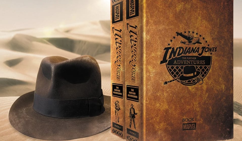 an image of a fedora and two volumes of the Indiana Jones: Further Adventures collection by Marvel against desert sand