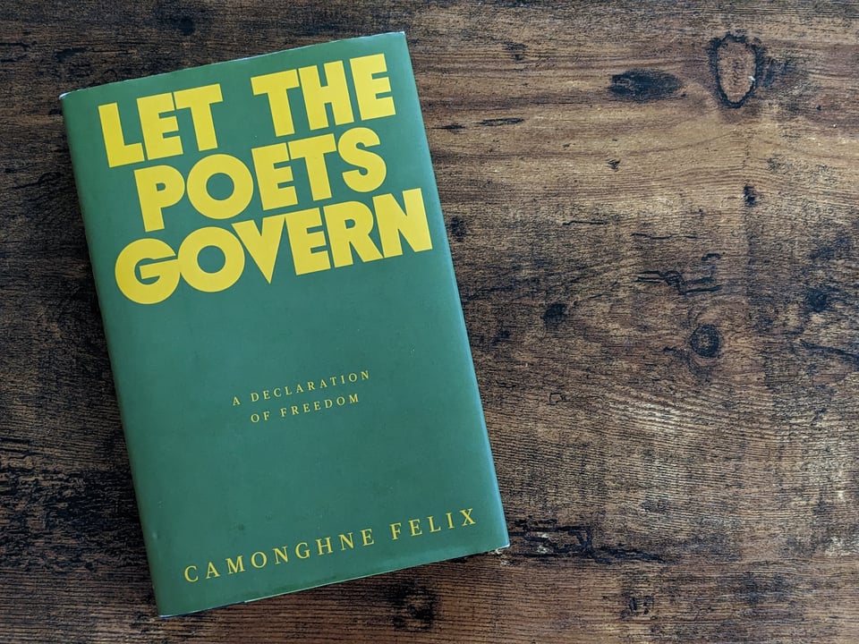 Let the Poets Govern, a declaration of freedom, by Camonghne Felix. In this photo, the book, with a forest green cover and yellow block lettering, sits on a wooden coffee table.
