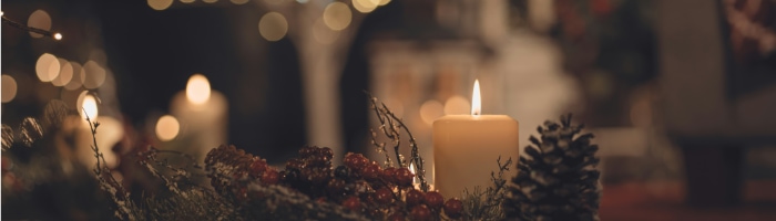 A candle next to a pine cone in front of a dark, blurry, twinkling background