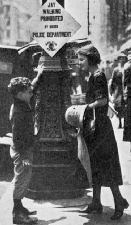 a woman and a child standing next to a street sign that reads: Jay walking prohibited by order of the Police Department