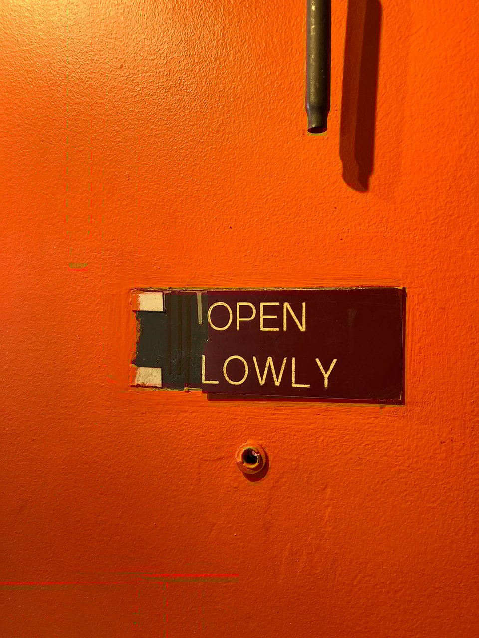 Orange door with a sign that reads: OPEN LOWLY. Photo by me.