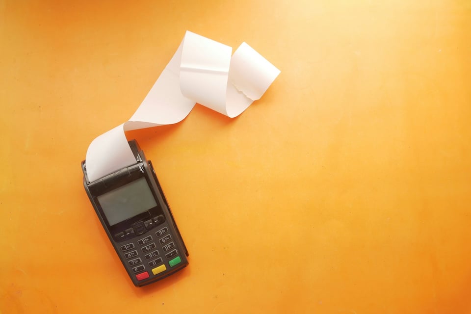 A handheld card-reader with a long receipt printing out of it.  Photo by Towfiqu barbhuiya on Unsplash.