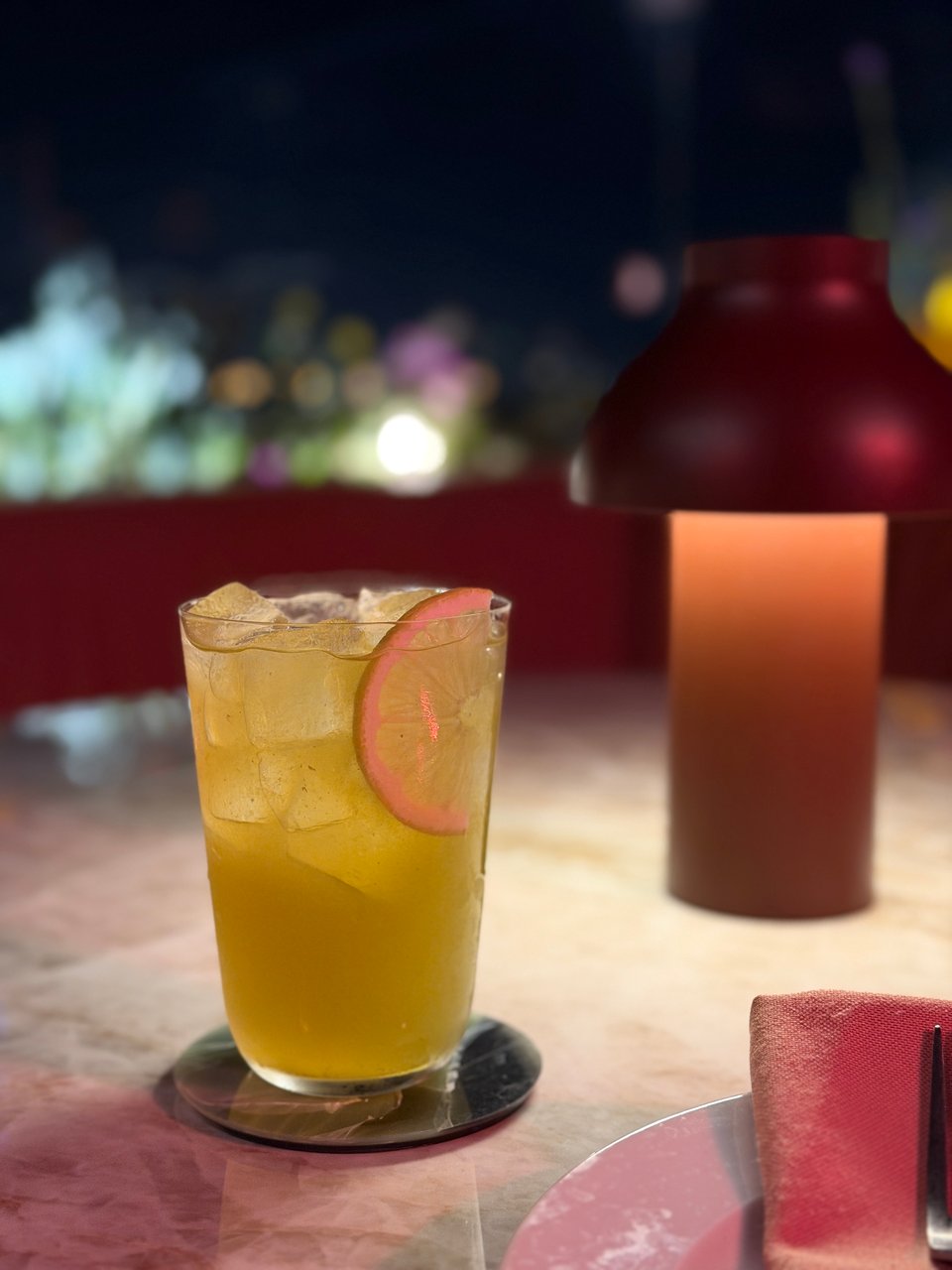 An orange tonic mocktail on an outdoor table with a small table lamp in the background.