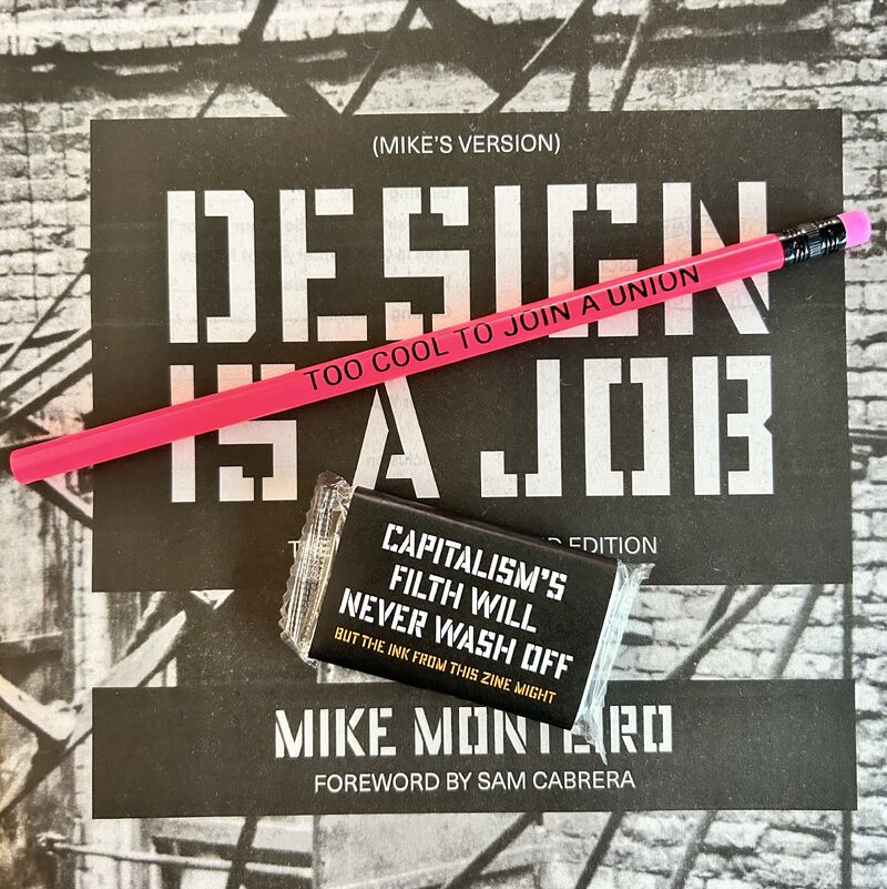 A pink pencil that says TOO COOL TO JOIN A UNION, and a little bar of soap with a label that says CAPITALISM’S FILTH WILL NEVER WASH OFF BUT THE INK FROM THIS ZINE MIGHT, sitting on top of a DESIGN IS A JOB zine.